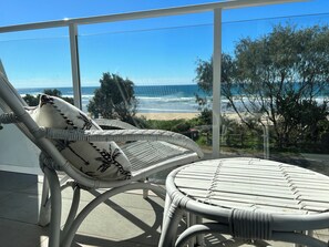 A balcony with wicker furniture, including a chair and a small table, overlooking a beach and ocean. - Premium Suite Ocean Views
(Lake Cathie)