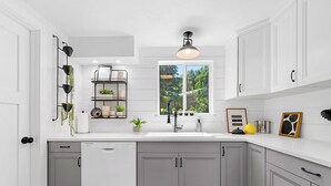 A kitchen with grey cabinets, a white countertop, a built-in sink, and a window with a view of greenery outside.