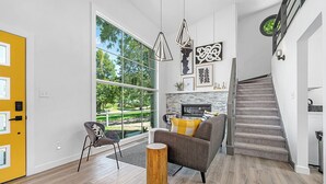A spacious living room with a large window, a fireplace, a staircase, and a yellow door.