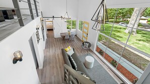 A spacious living area with a large window, a gray sofa, a dining table, and a staircase.