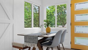 A dining area with a table, chairs, a plant, and a window with a view of trees.