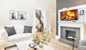 Ein modernes Wohnzimmer mit einem weißen Sofa, einem Kamin und einem darüber angebrachten Fernseher.