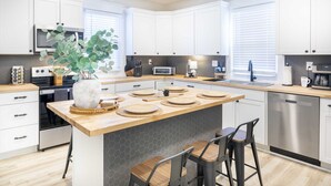 Una cocina moderna con armarios blancos, una isla central con taburetes, un microondas, un tostador y un lavamanos.