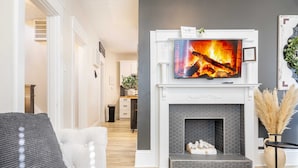 Una sala de estar con chimenea, televisor montado encima y un sofá.