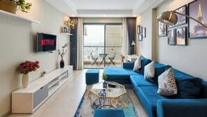 A modern living room with a blue sofa, a glass coffee table, and a flat-screen TV mounted on the wall. - Gold View Saigon Riverside (Ho Chi Minh City)