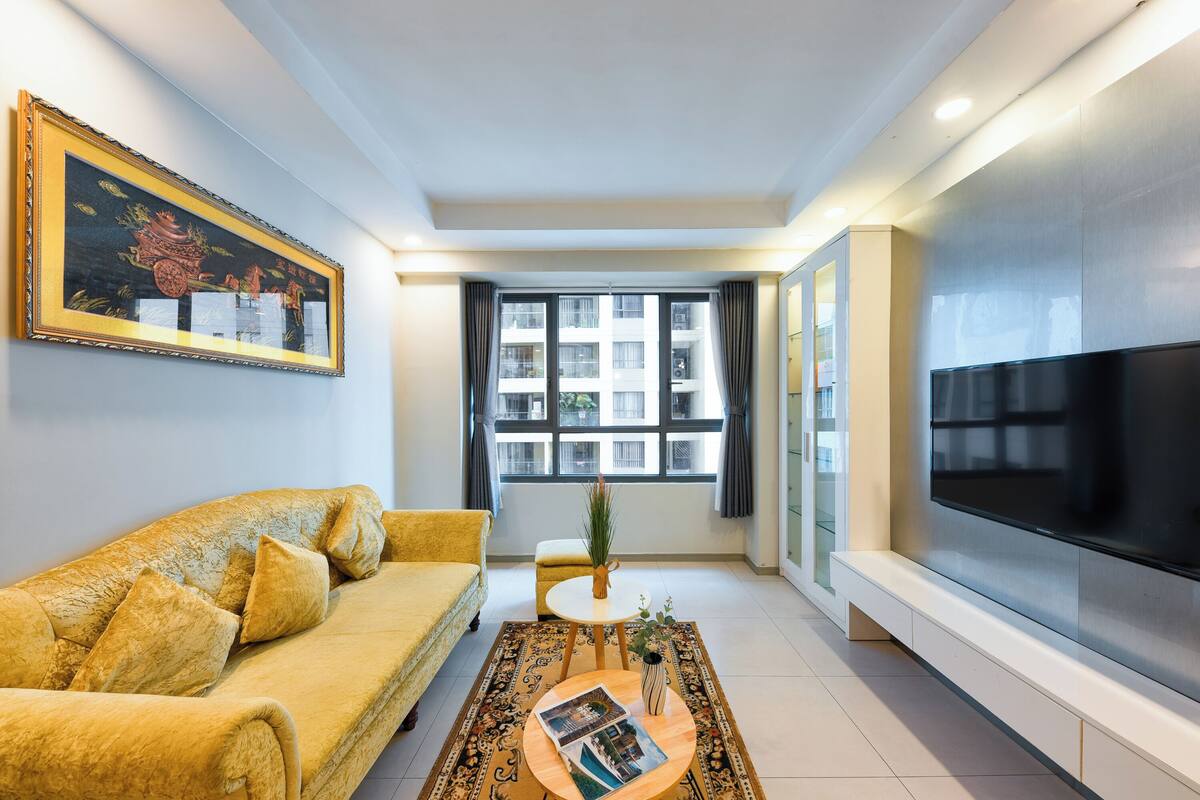 A modern living room with a sofa, a coffee table, a TV, and a large window.