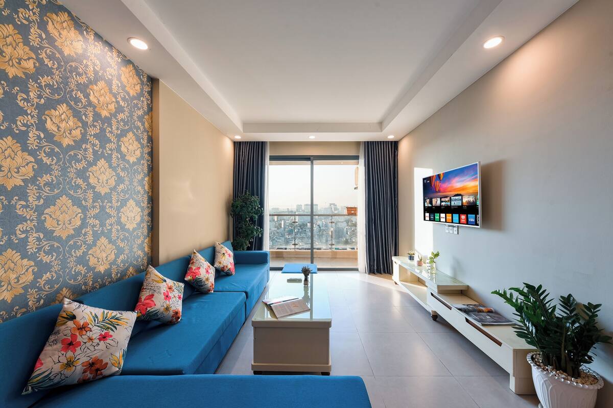 A modern living room with a blue sofa, a coffee table, and a TV mounted on the wall.