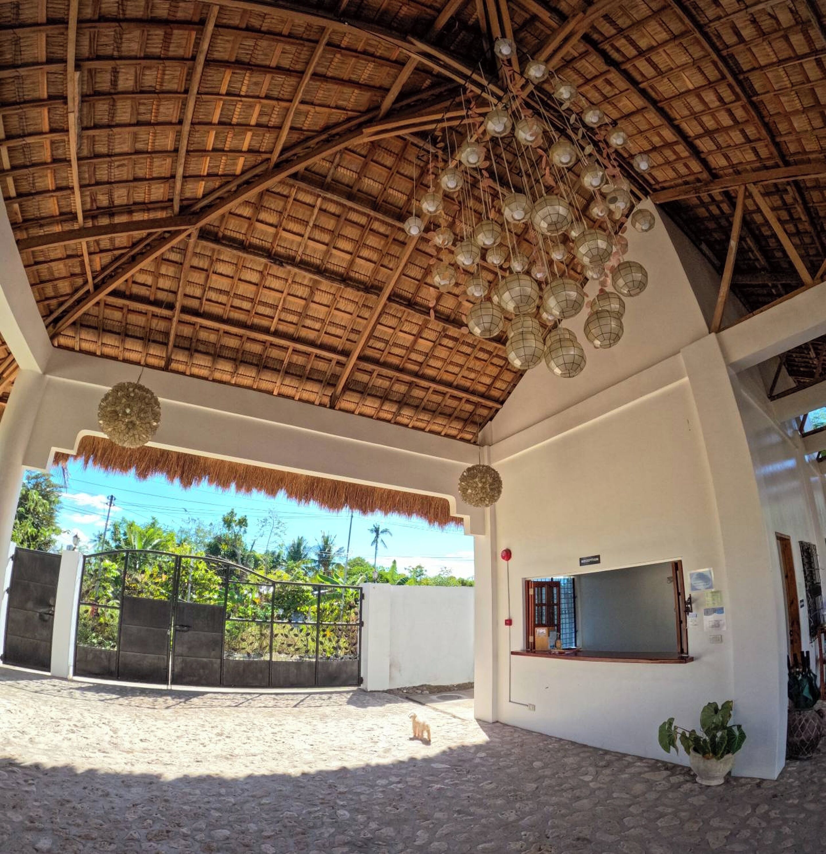 A covered outdoor area with a thatched roof, hanging lanterns, and a reception desk.