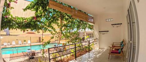 A balcony with a view of a swimming pool, outdoor furniture, and a railing.
