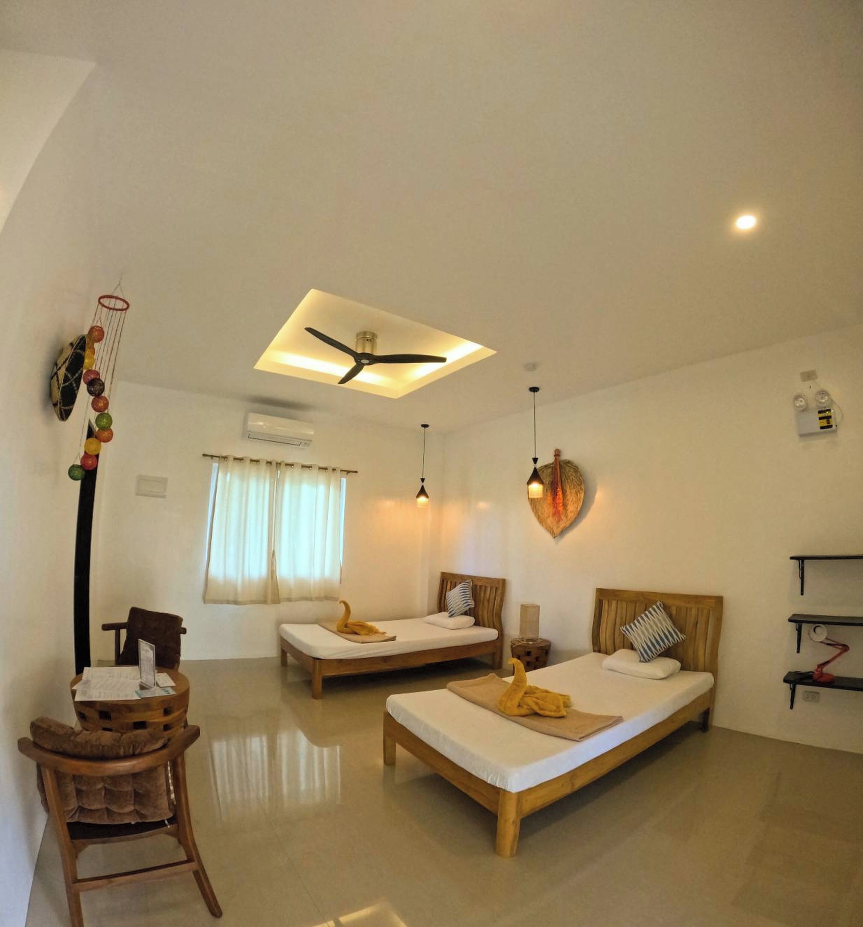 A hotel room with two beds, a desk, a chair, a ceiling fan, and a heart-shaped wall decoration.