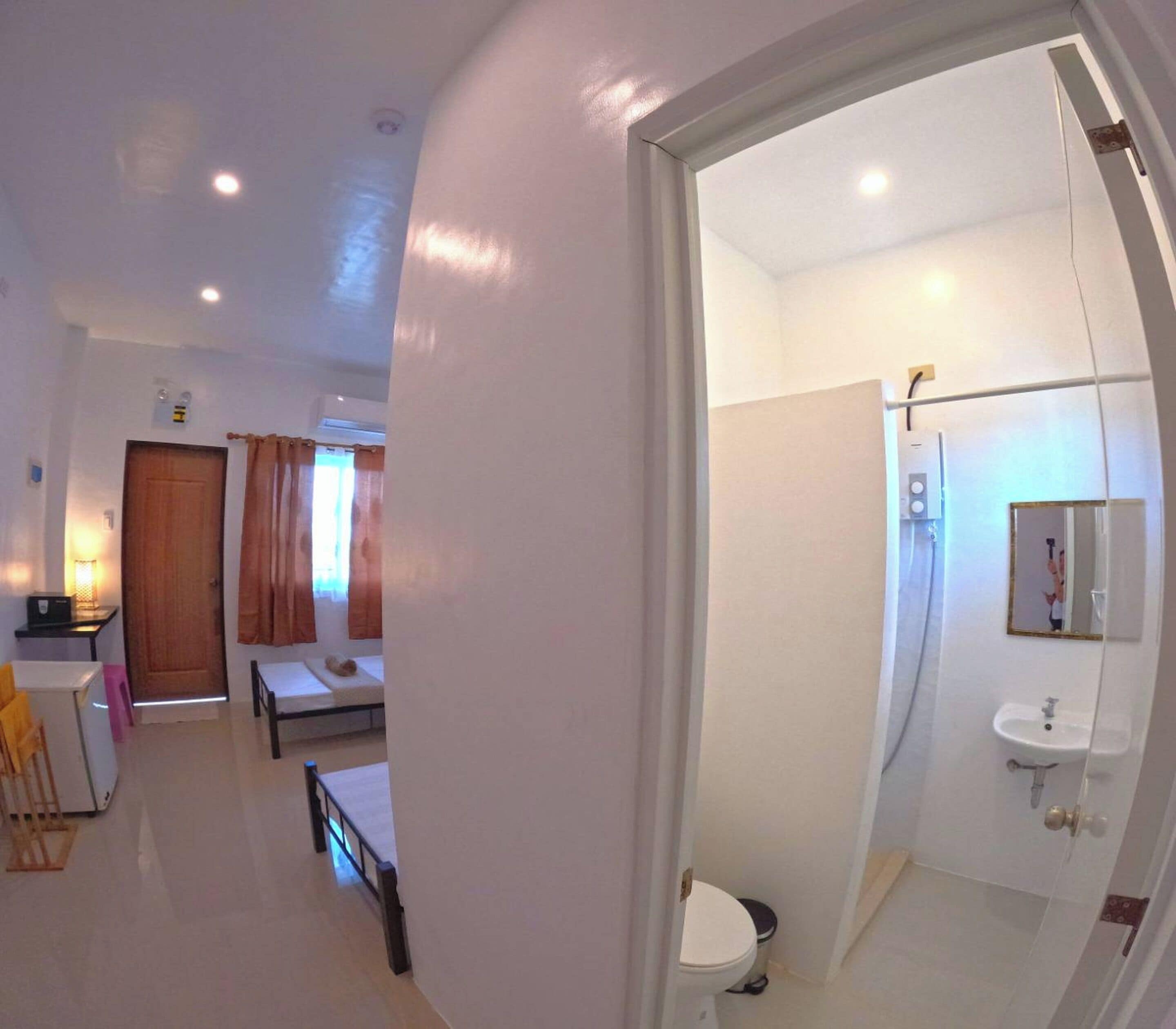 A compact hotel room with a bed, a small desk, a chair, a sink, and a mirror.