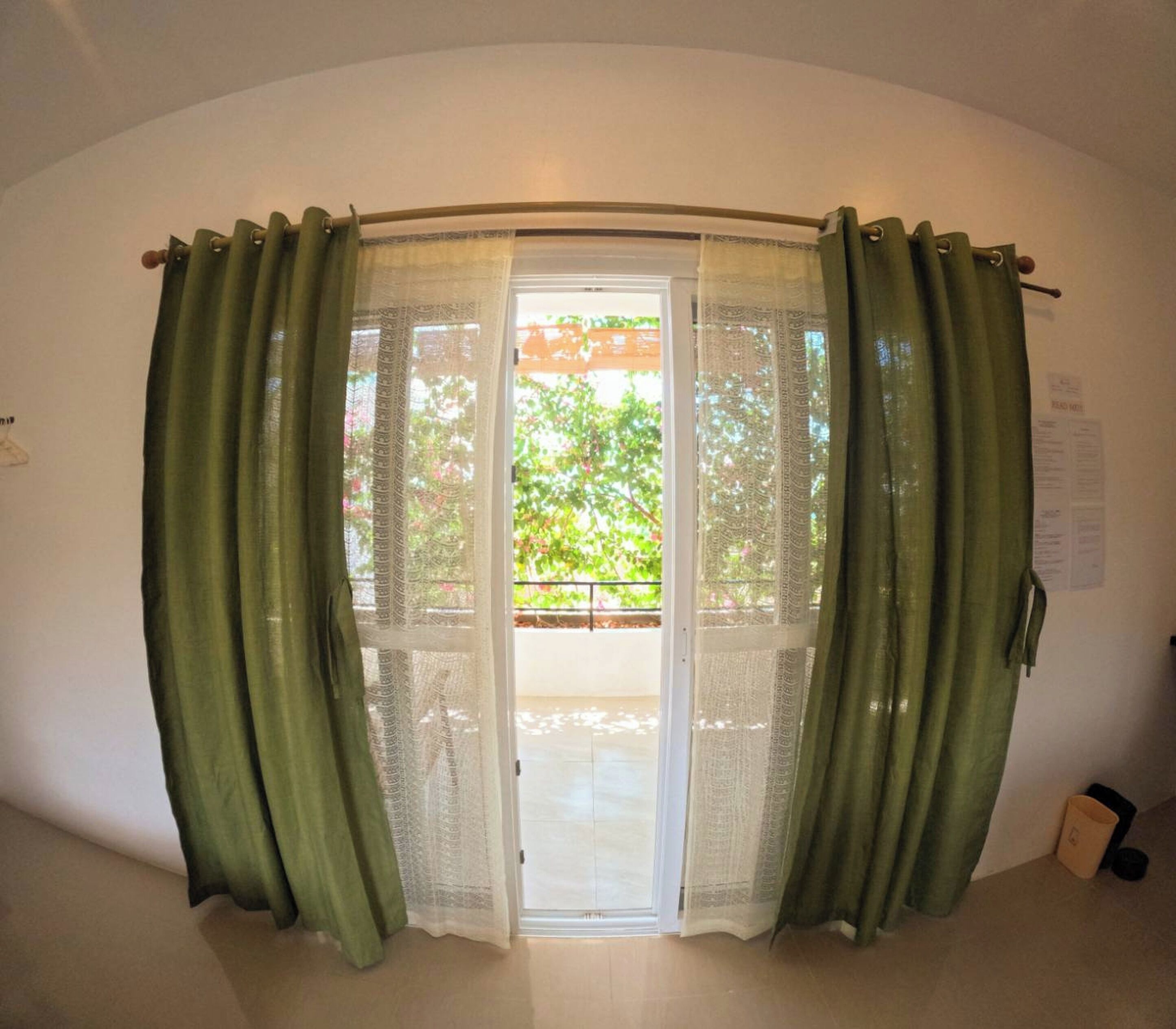 Una habitación con puerta corrediza de vidrio que da a un balcón con vistas a árboles y un edificio.