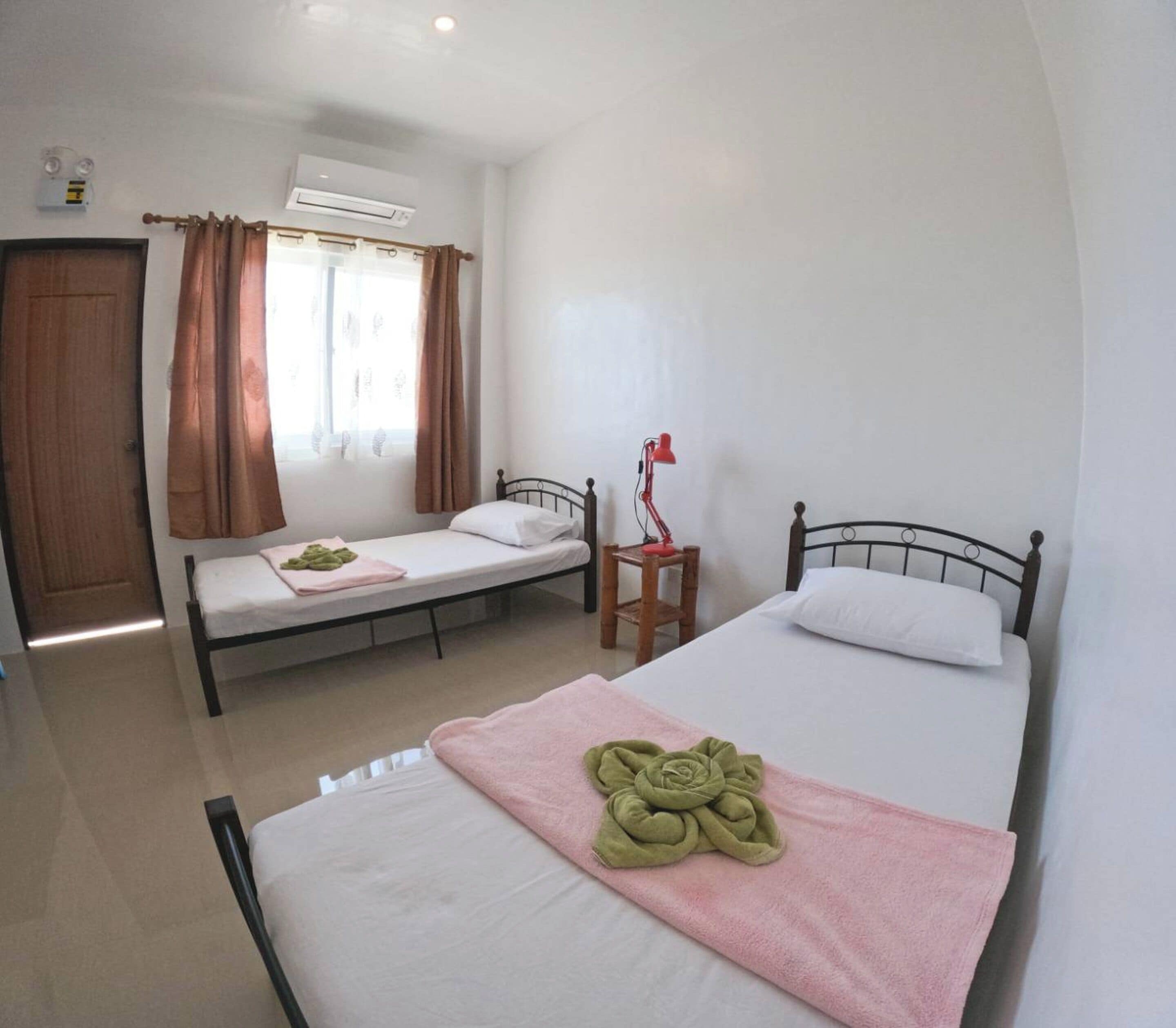 Une chambre d’hôtel avec deux lits simples, un bureau avec une chaise, une fenêtre avec des rideaux et un appareil de climatisation.