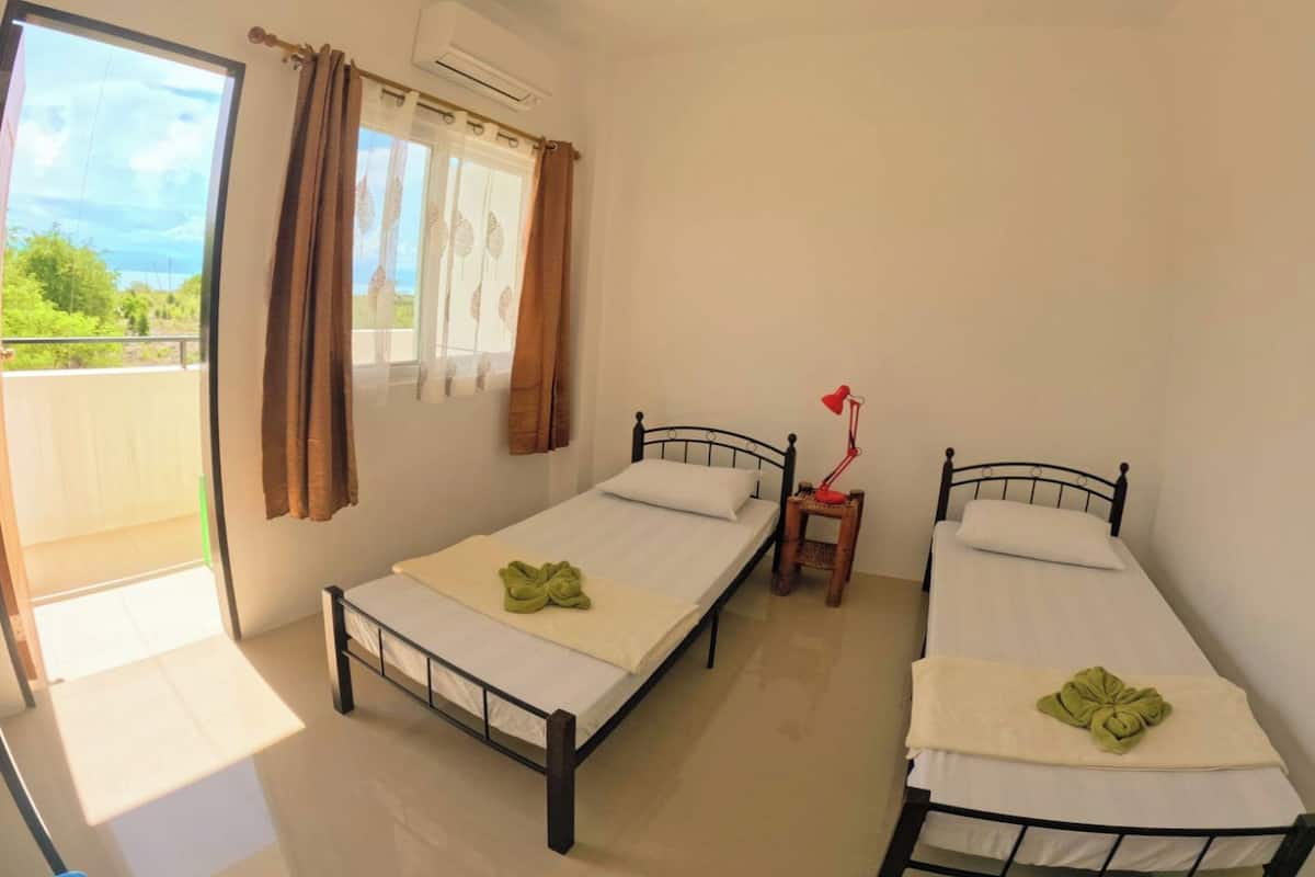Un dormitorio con dos camas individuales, una mesita de noche pequeña con lámpara y una ventana con cortinas.