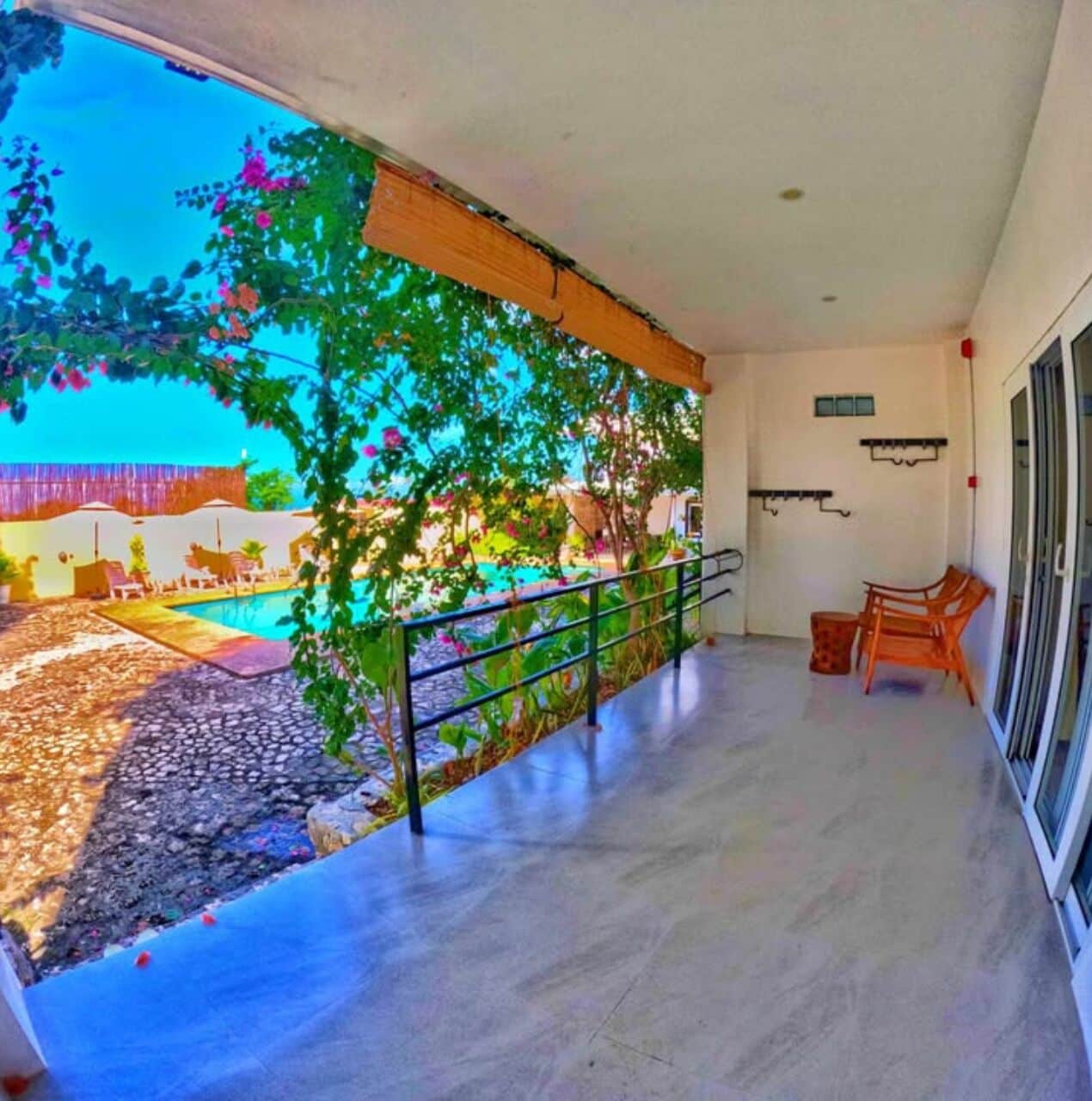 A balcony with a view of a pool and garden, a chair, and a small table.