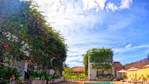 A swimming pool with a stone border, surrounded by potted plants and a thatched-roof building.
