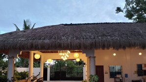 A thatched-roof structure with a covered entrance, potted plants, and a motorcycle parked outside.
