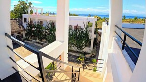A balcony with a view of a coastal landscape, including a white building and a thatched-roof structure.