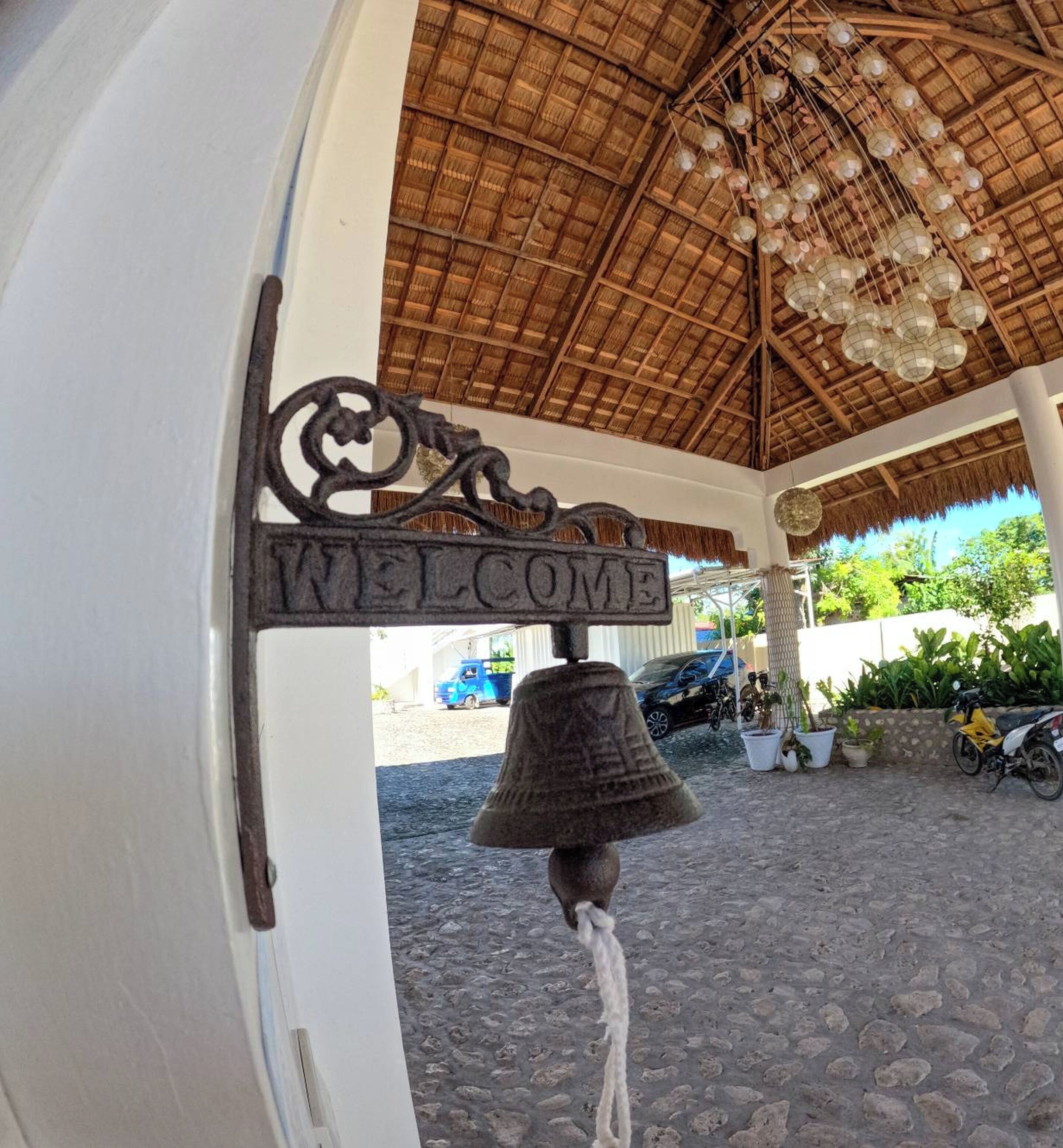 A bell with a 'WELCOME' sign hanging from a structure with a thatched roof.
