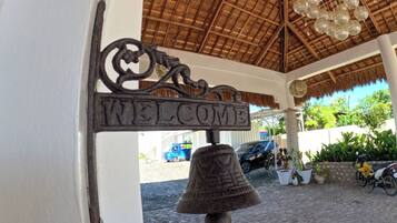 A bell with a 'WELCOME' sign hanging from a structure with a thatched roof.