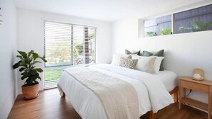 Ein Schlafzimmer mit einem großen Bett, weißer Bettwäsche, einem Blumentopf und einem Fenster mit Jalousien.