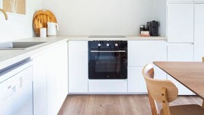 Eine moderne Küche mit weißen Schränken, einem eingebauten Ofen und einem Holzes Esstisch mit einem Stuhl.