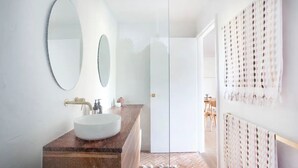 Ein Badezimmer mit einem weißen Waschbecken, zwei Spiegeln und einer Holzkommode.