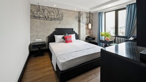 Una habitación de hotel moderna con una cama grande, un escritorio pequeño, una mesita de noche, una ventana con cortinas y vistas a la ciudad.
