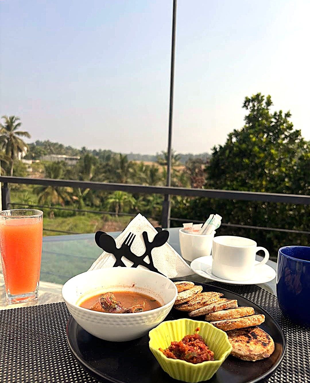 A table with a meal consisting of soup, bread, and a drink, set against a scenic view.