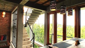 Eine Treppe führt zu einem Balkon mit Blick auf Grünflächen, einem Tisch mit Platzsetzer und hängenden Lichtern mit Schrift.