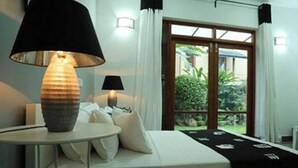 Ein Schlafzimmer mit einem Bett, zwei Nachttischlampen, einem kleinen runden Tisch mit einer Lampe und Blick ins Grüne durch eine Glastür.