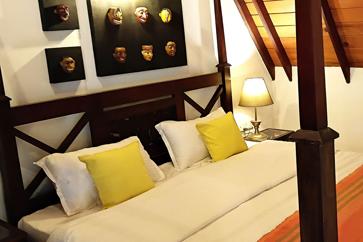 Une chambre à coucher avec un lit à baldaquin, une table de chevet avec une lampe et un mur orné de tableaux encadrés.