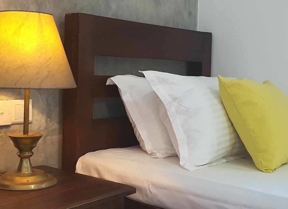 A neatly made bed with white and yellow pillows, a wooden headboard, and a bedside lamp on a wooden nightstand.