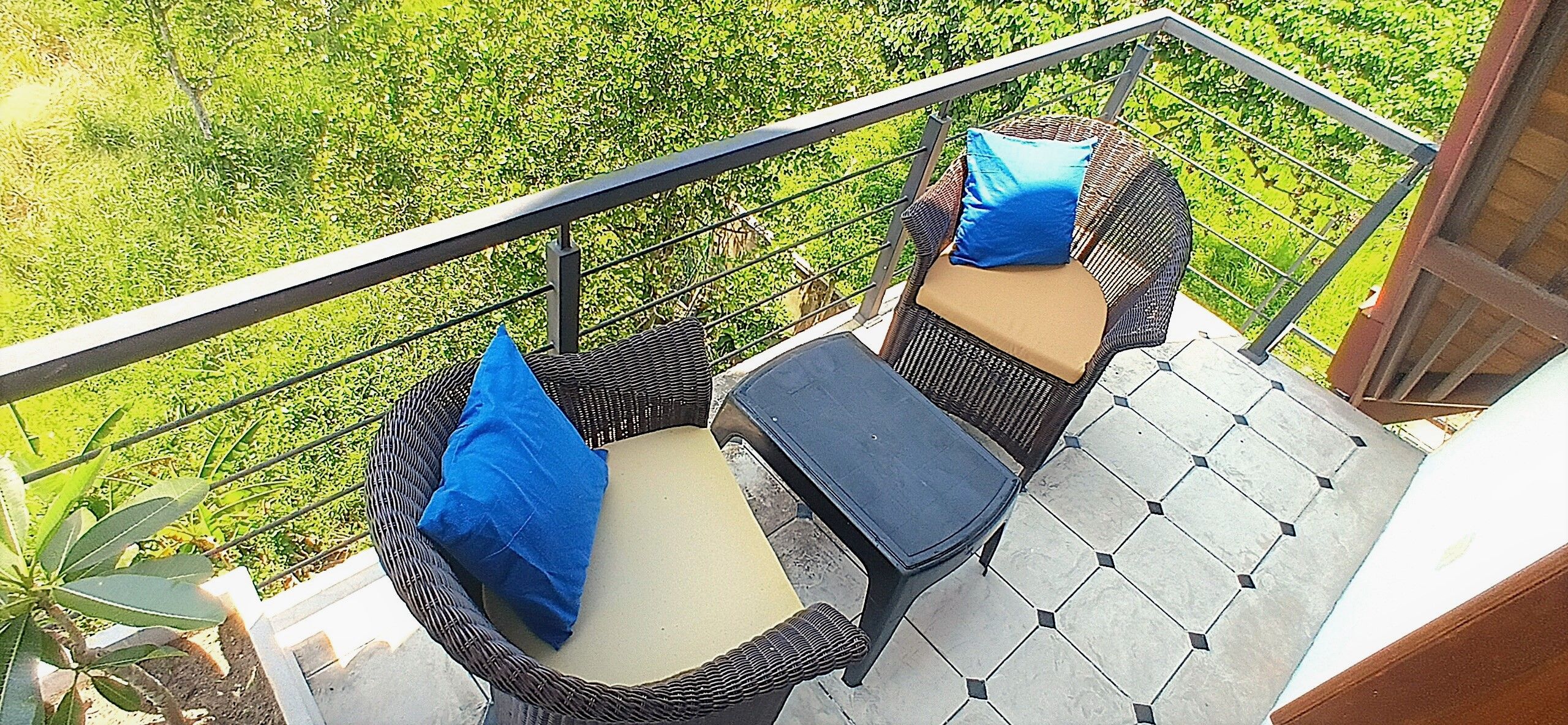 A balcony with wicker furniture, two cushions, and a view of greenery.