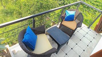 A balcony with wicker furniture, two cushions, and a view of greenery.