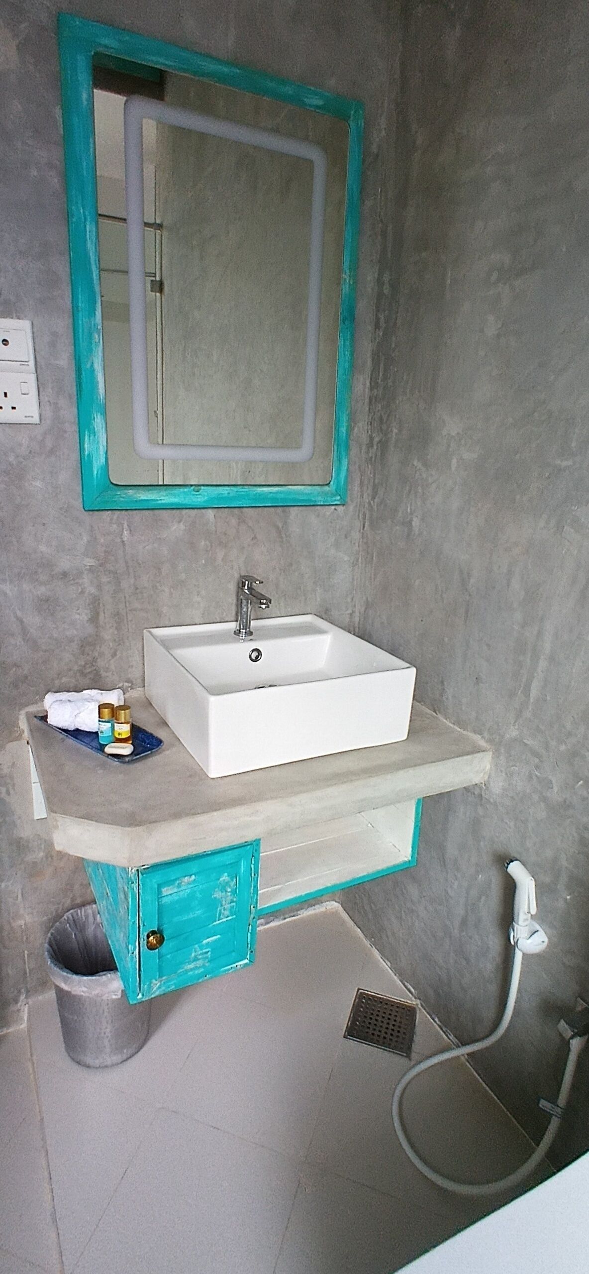 Un baño con un lavamanos blanco, un espejo con marco verde azulado, una toalla y un bote de basura.
