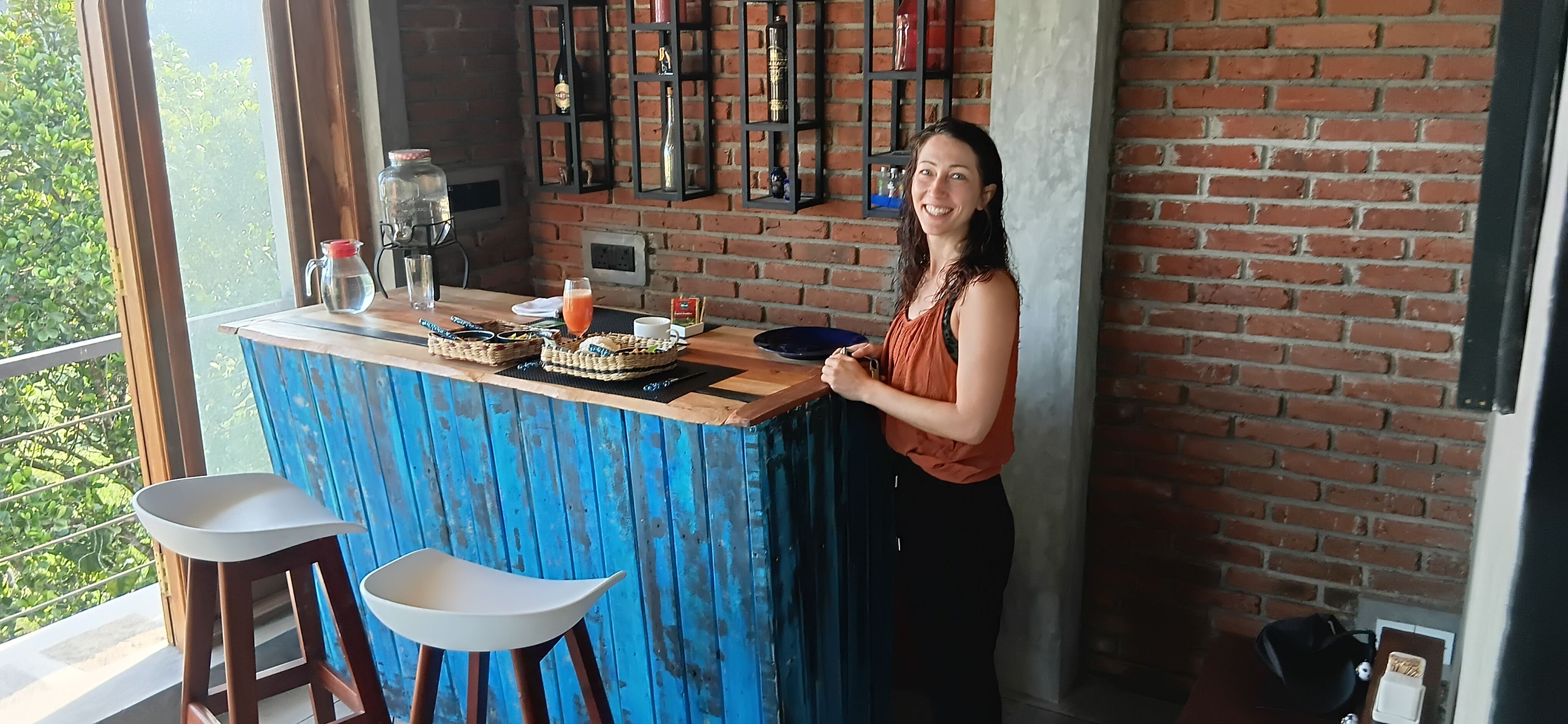 A bar area with a blue-painted counter, stools, and a brick wall backdrop.