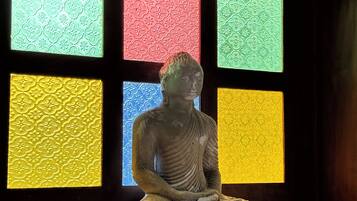 Una estatua de una figura sentada en posición meditativa, ubicada en un estante con dos cuencos a cada lado.