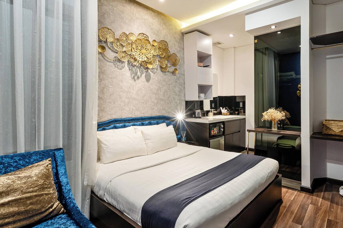 Une chambre d’hôtel moderne, dotée d’un grand lit, d’un bureau, d’une armoire et d’une salle de bain visible à travers une porte ouverte.