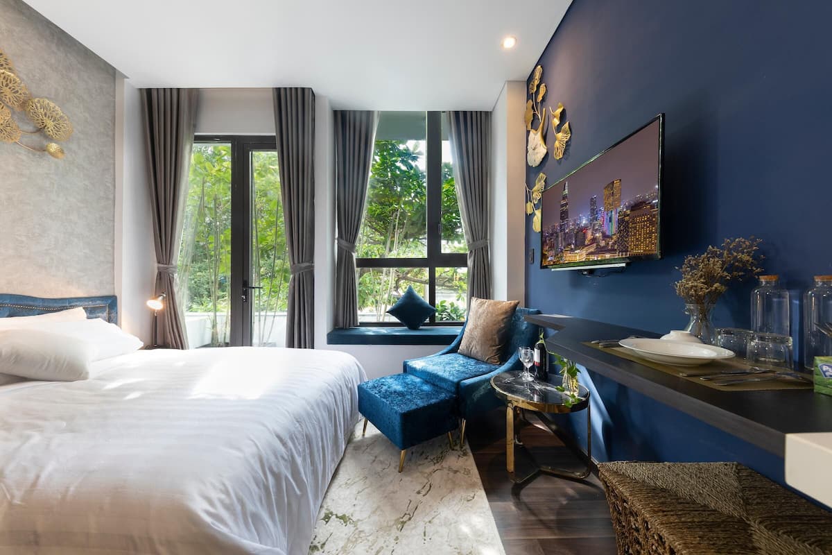 Une chambre d’hôtel moderne avec un grand lit, un canapé bleu, un coin repas et un tableau représentant un paysage urbain accroché au mur.