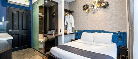 A modern hotel room with a large bed, a walk-in closet, and a bathroom with a glass door.