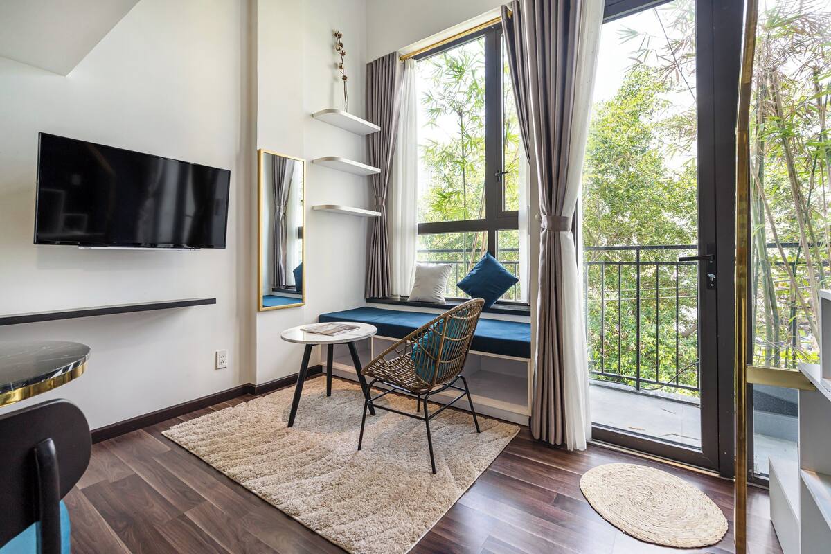 Un salon moderne avec un téléviseur à écran plat, un canapé placé près d’une grande fenêtre, une petite table ronde et un fauteuil en osier.