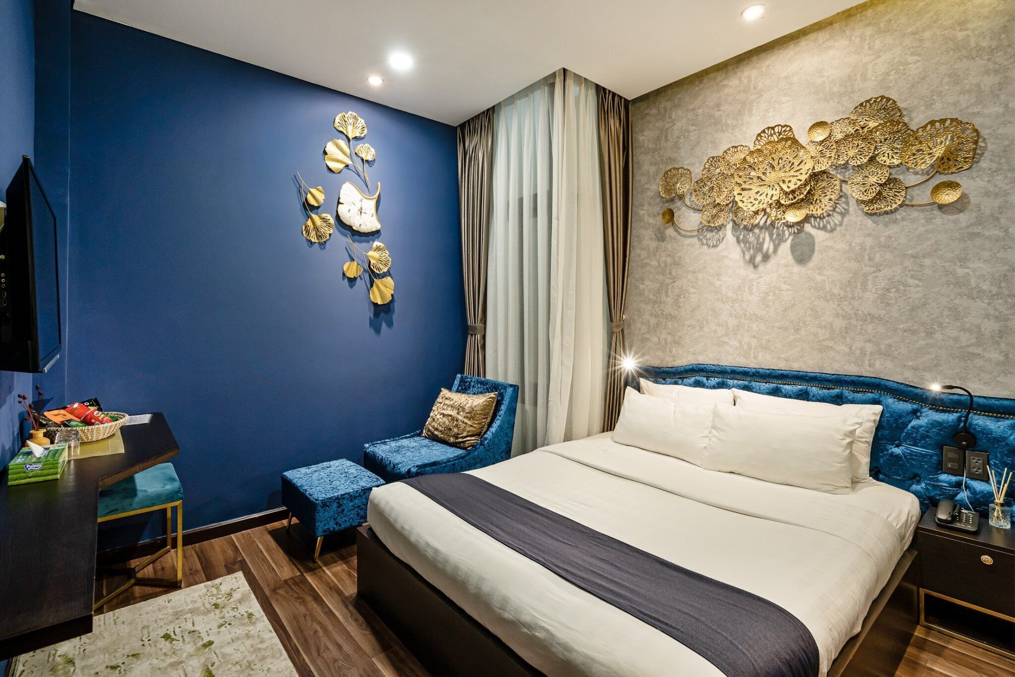 A modern bedroom with a large bed, a blue chair, a small table with a basket, and decorative wall art.