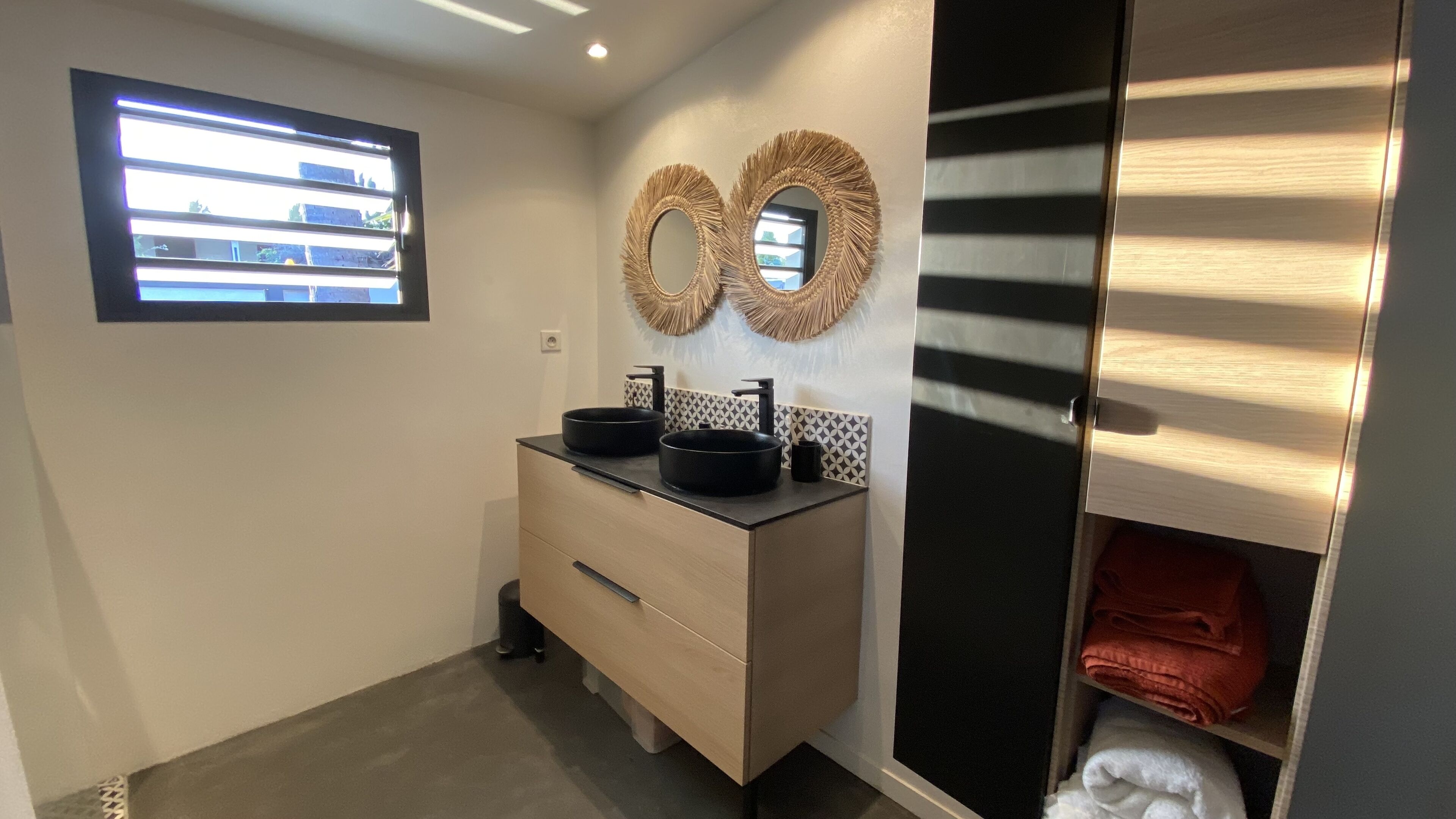 A modern bathroom with a double sink vanity, a window with blinds, and a mirror with a decorative frame.