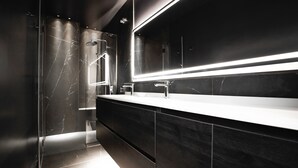 A modern bathroom with a dark marble vanity, a large mirror, and a glass shower enclosure.