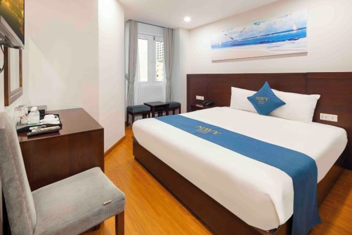 A hotel room with a large bed, a desk, a chair, and a window with curtains.