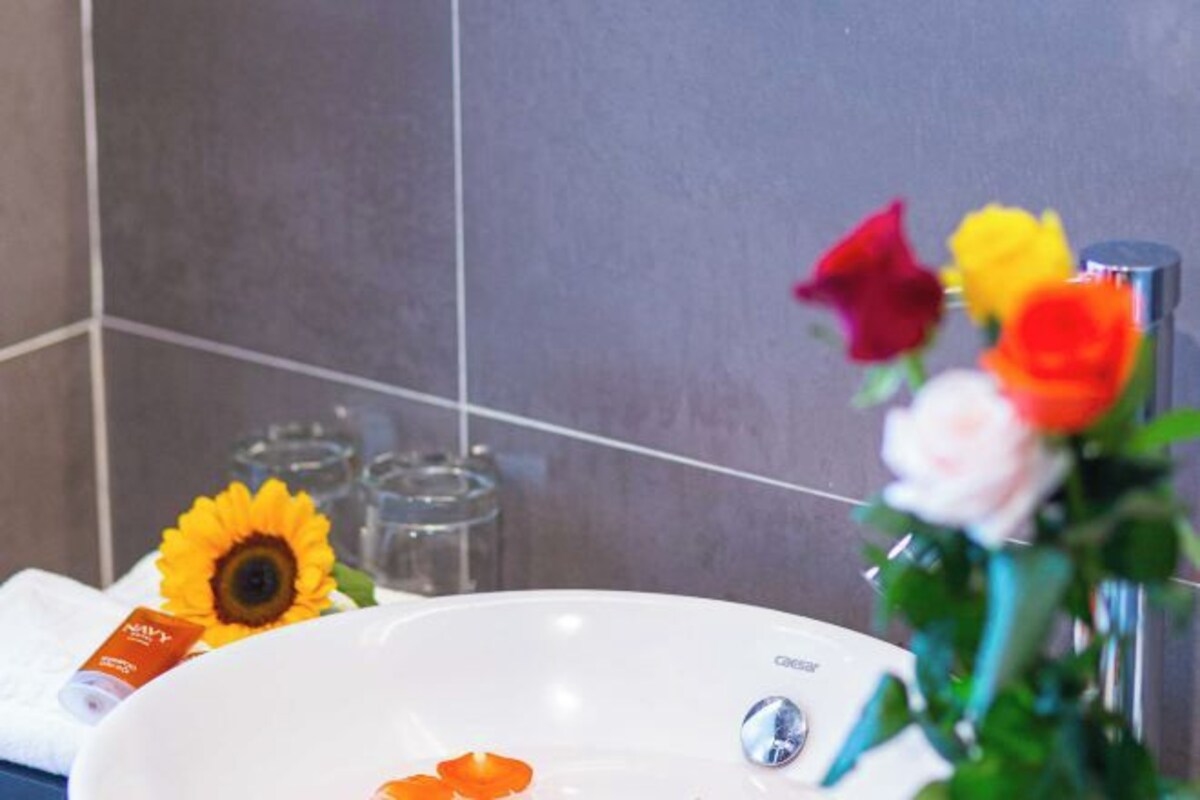 A bathroom with a white sink, a mirror, and a vase with colorful flowers.