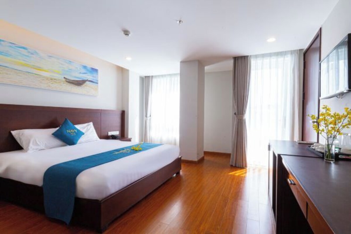 A hotel room with a large bed, a desk, and a painting on the wall.