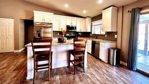 A modern kitchen with white cabinets, stainless steel appliances, and a central island with two chairs. - Spacious, FREE Private Heated Pool, Great Location! 10+ Guests & Pet Friendly (Mesa)