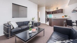 A modern living room with a black leather sofa, a coffee table, and a dining area with a small island. - The Vibe: Auckland CBD
 (Auckland)
